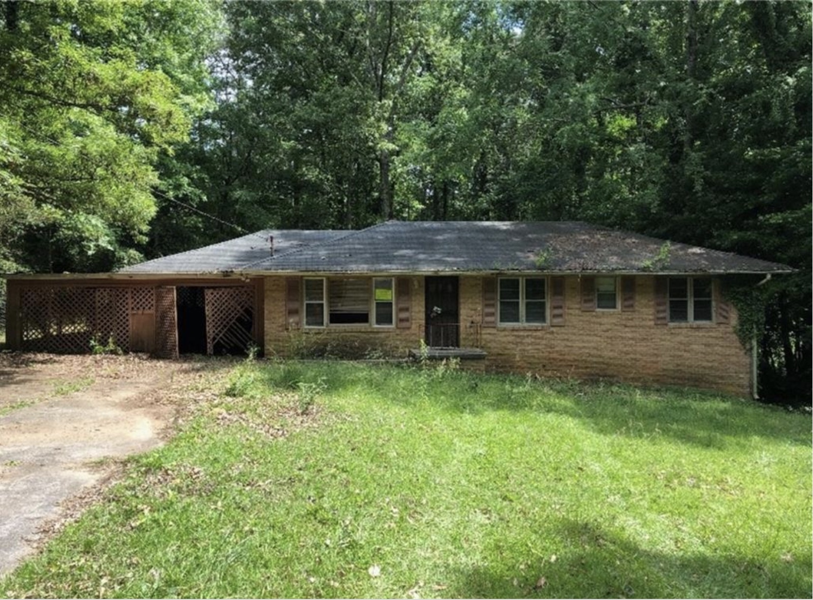 Distressed brick ranch house in Metro Atlanta before renovation, overgrown yard and worn roof